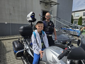 na zdjęciu chłopczyk na motocyklu policyjnym z boku stoi policjant