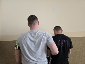 na zdjęciu zatrzymany mężczyzna z policjantem stoją tyłem