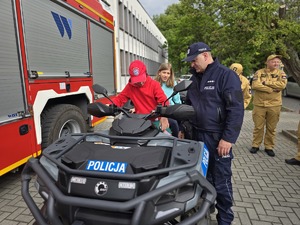 na zdjeciu dziecko na quadzie obok stoi policjant
