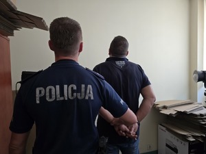 na zdjęciu policjant z mężczyzna który stoi tyłem w kajdankach