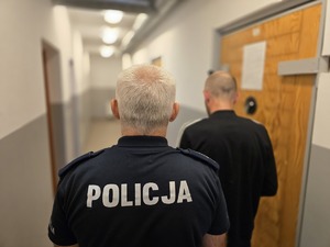 na zdjęciu policjant z zatrzymanym stoją tyłem