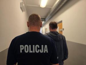 na zdjęciu zatrzymany z policjantem stoją tyłem