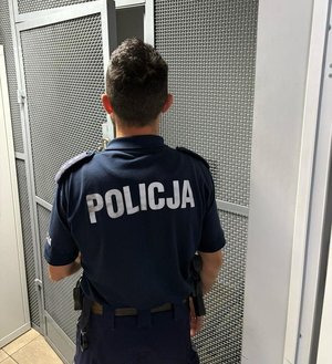 na zdjęciu policjant stoi tyłem i krata