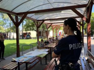 na zdjęciu policjant oraz uczestnicy półkolonii w tle