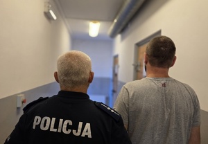 na zdjęciu policjant z zatrzymanym stoją tyłem