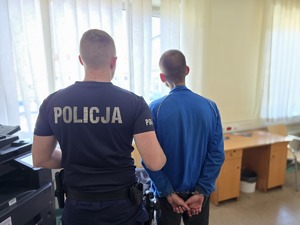 na zdjęciu policjant i sprawca stoją tyłem sprawca w kajdankach