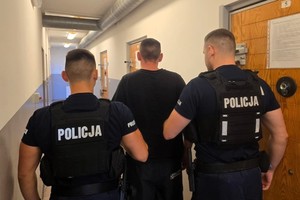 Zdjęcie kolorowe przedstawiające policjantów prowadzących zatrzymanego mężczyznę.