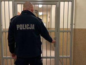 na zdjęciu policjant stoi tyłem przy kracie z więzienia