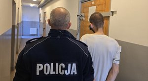 na zdjęciu zatrzymany z policjantem stoją tyłem