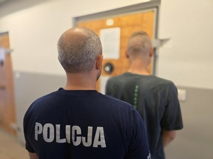 na zdjęciu zatrzymany z policjantem stoją tyłem