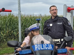 na zdjęciu policjant ruchu drogowego obok motocykl i na nim dziewczynka