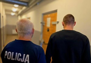 na zdjeciu zatrzymany z policjantem stoją tyłem