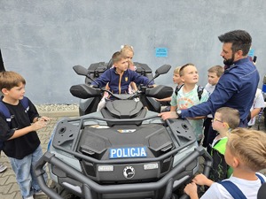 na zdjęciu dzieci na quadzie obok stoi policjant