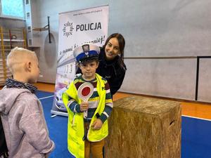 na zdjęciu policjantka pomaga chłopcu ubrać czapkę kamizelkę policyjna