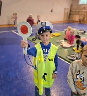 na zdjęciu chłopczyk w kamizelce i czapce policyjnej trzyma tarcze