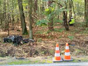 na zdjęciu roztrzaskany motocykl dwa pachołki na drodze i policjanci w lesie
