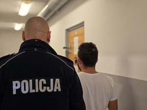 na zdjęciu zatrzymany stoi tyłem z policjantem