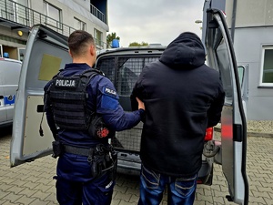 na zdjęciu zatrzymany mężczyzna z policjantem tyłem