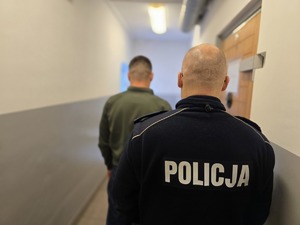 na zdjęciu policjant stoi tyłem z zatrzymanym