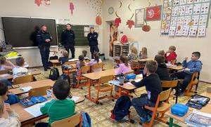 na zdjęciu policjanci prowadza pogadankę na temat bezpieczeństwa dzieci siedzą w ławkach