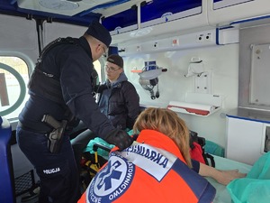 na zdjęciu widać jak policjant pomaga osobom poszkodowanym w wypadku jest w środku karetki