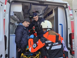 na zdjęciu widać jak policjant pomaga osobom poszkodowanym w wypadku na zewnątrz stoi juz ratowniczka medyczna
