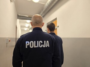 na zdjęciu zatrzymany z policjantem stoja tyłem