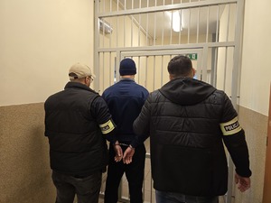 na zdjeciu policjanci stoja tyłem z zatrzymanym