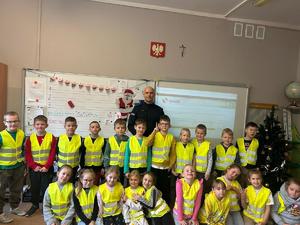 na zdjęciu policjant i dzieci w kamizelkach odblaskowych