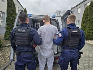 na zdjęciu zatrzymany i policjanci stoi tyłem